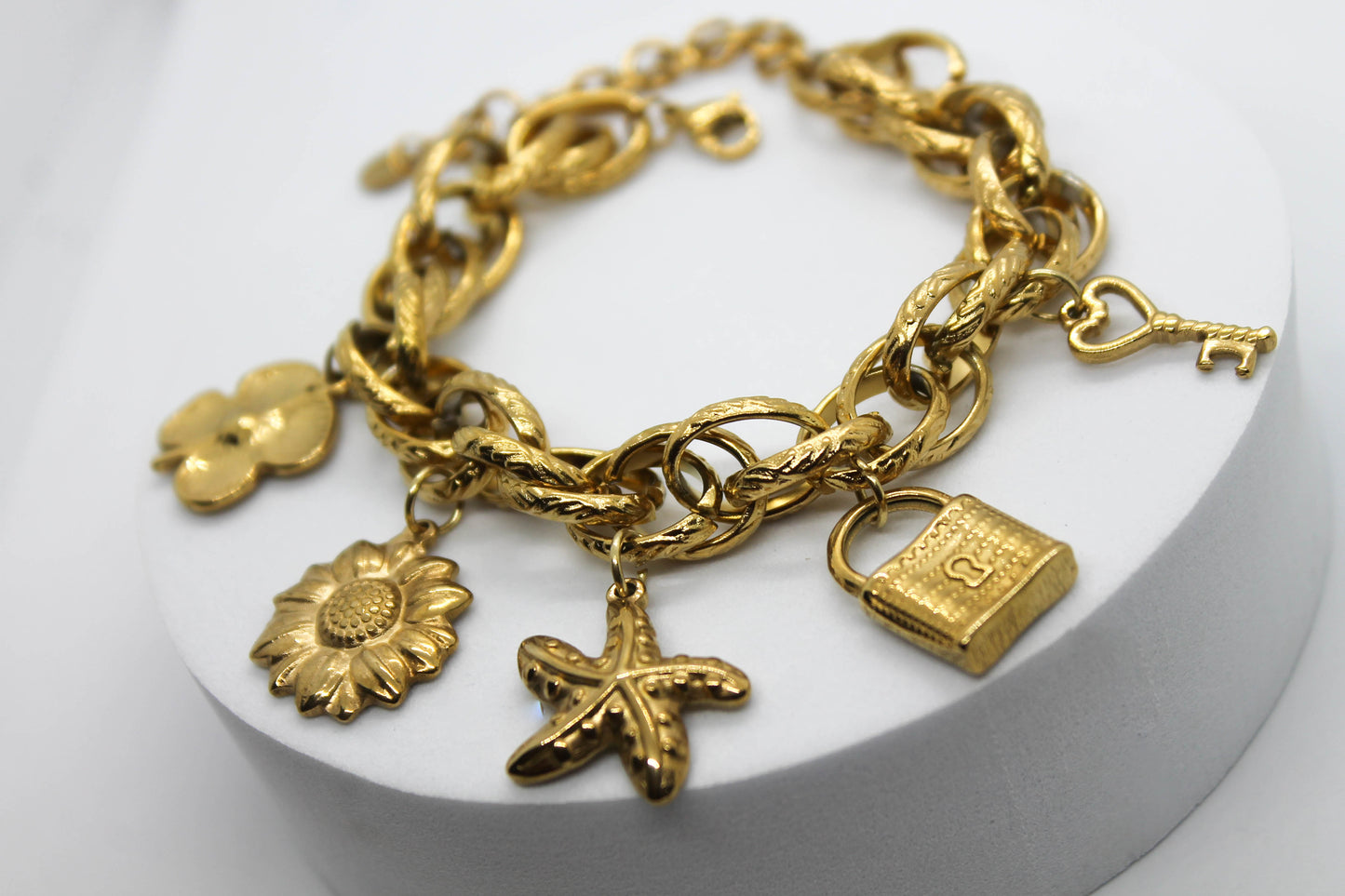 PULSERA DIJES COLGANTES FLOR, GIRASOL, ESTRELLA DE MAR, CANDADO, LLAVE; TONO DORADO