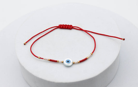 PULSERA TEJIDA HILO ROJO, OJO AZUL PLANO CHAQUIRA BLANCA Y ROJA